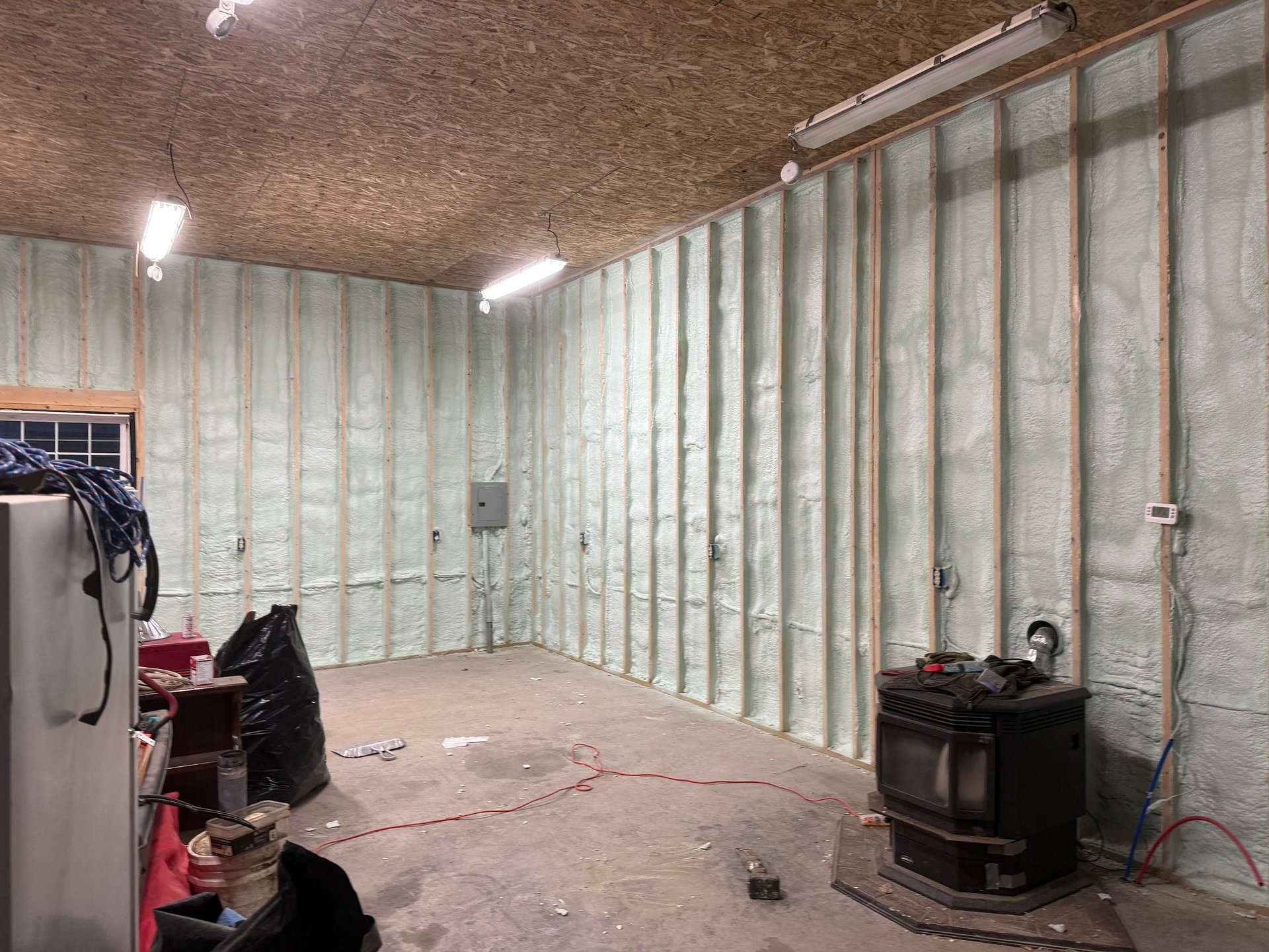 Interior of a workshop or garage with white insulated walls, industrial lighting, and equipment including hoses and tools scattered on the floor