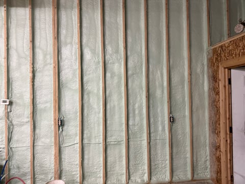 Interior wall with foam insulation batts between wooden studs and a wooden door frame on the right side