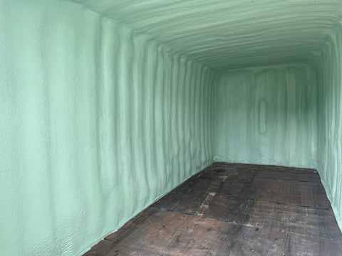 Interior of an empty shipping container with mint green metal walls and dark floor, showing perspective toward the far end